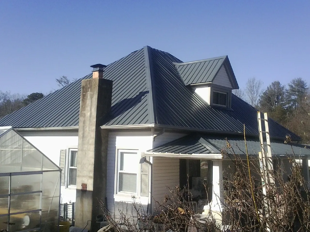 Dark blue standing seam metal roof on a white farmhouse with dormer — Slate & Tile Roof Repair by Roofing Brothers in Luxemburg