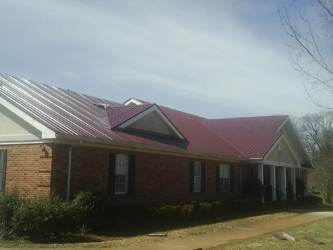 Red metal roof with gabled entries on a long brick building, from a Hail Damage Roof Repair job in Luxemburg