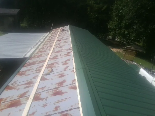 Old rusted panels beside newly installed green metal roofing — Wind Damage Roof Repair by Roofing Brothers in Luxemburg