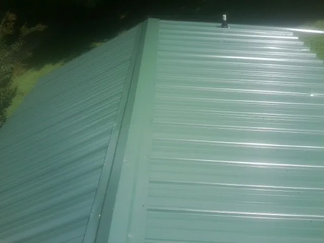 New green metal panels meeting at the ridge of a roof — Flat Roof Repair work by our crew in Luxemburg
