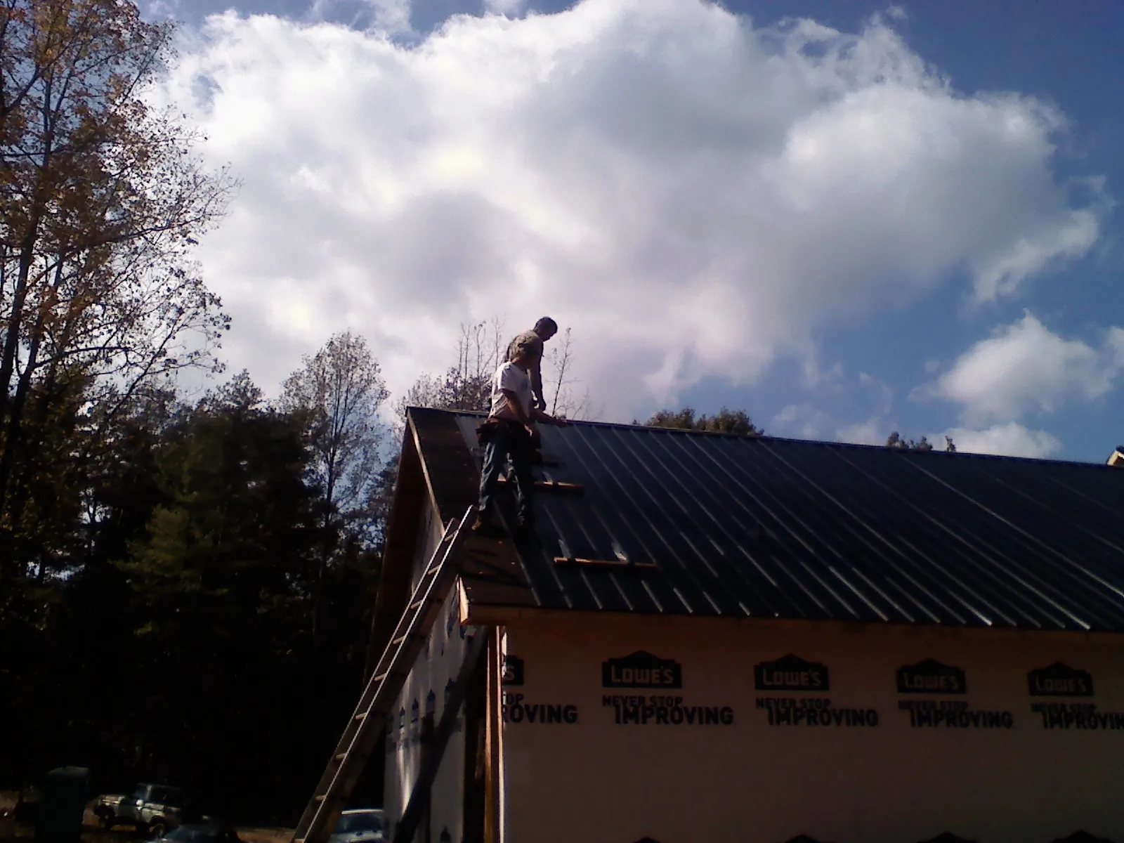 Roofer fastening dark metal panels high against a cloudy sky, from a Roof Inspection job in Luxemburg