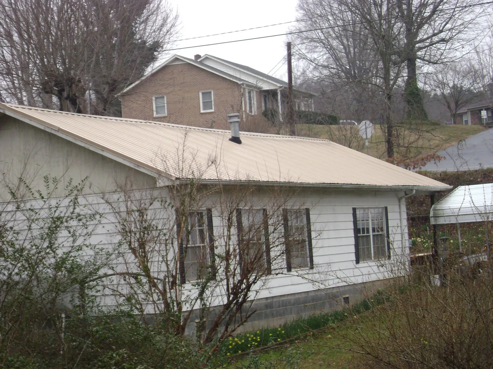 Tan metal roof on a white sided house set into a hillside — Commercial Roofing by Roofing Brothers in Luxemburg